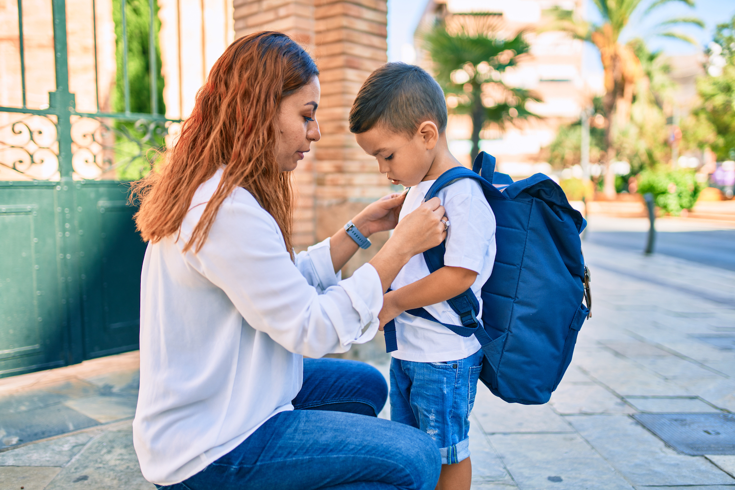 Latin mother putting up backpack her student son at the city.